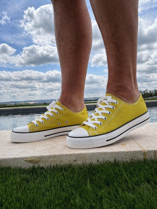 Chaussures sneakers femme jaunes, baskets basses en toile, lacets blancs, vues par les pieds sur fond d’herbe et ciel nuageux. Baskets Basses Toile Vert Moutarde à l’honneur.