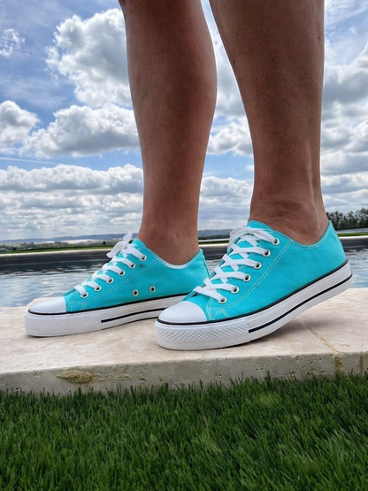 Chaussures Converse bleu turquoise esprit baskets basses posées sur une bordure en pierres près d’un jardin et d’un ciel nuageux.