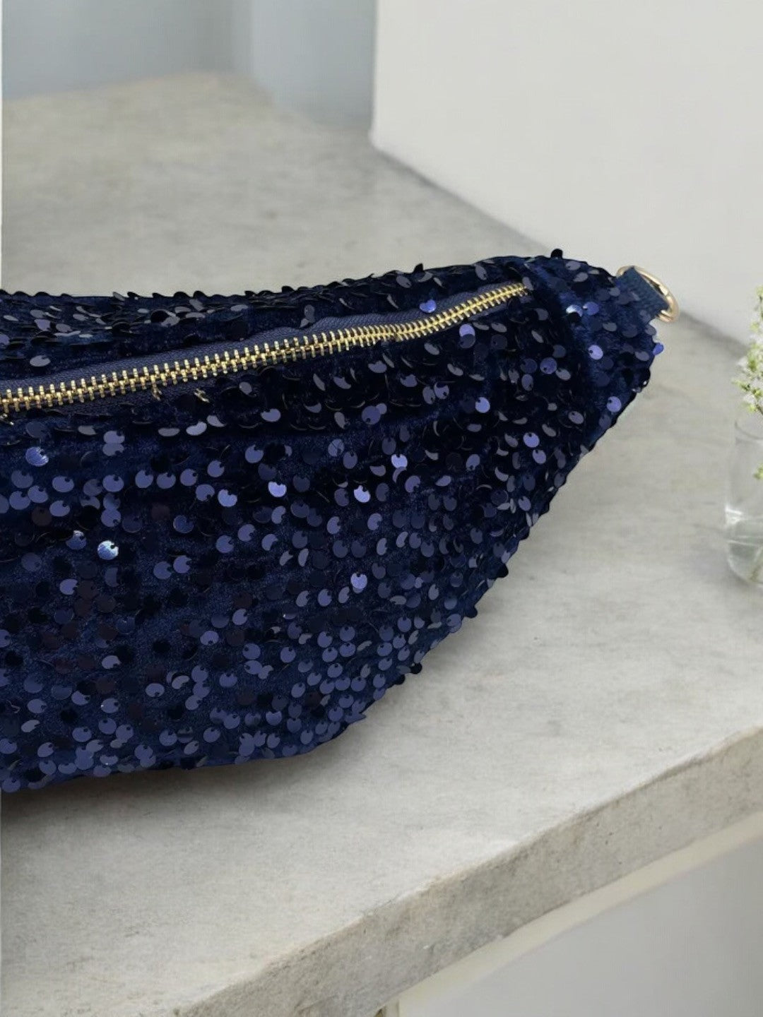 Sac banane en paillettes bleu marine avec fermeture éclair dorée et bandoulière réglable, vue en détail sur le dessus.