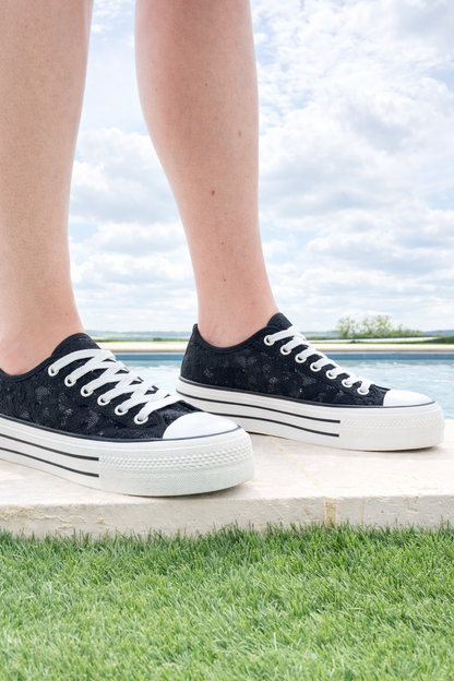 Chaussures baskets noires à dentelle, platforme épaisse, semelles blanches à rayures, lacets blancs, vue des pieds en extérieur.