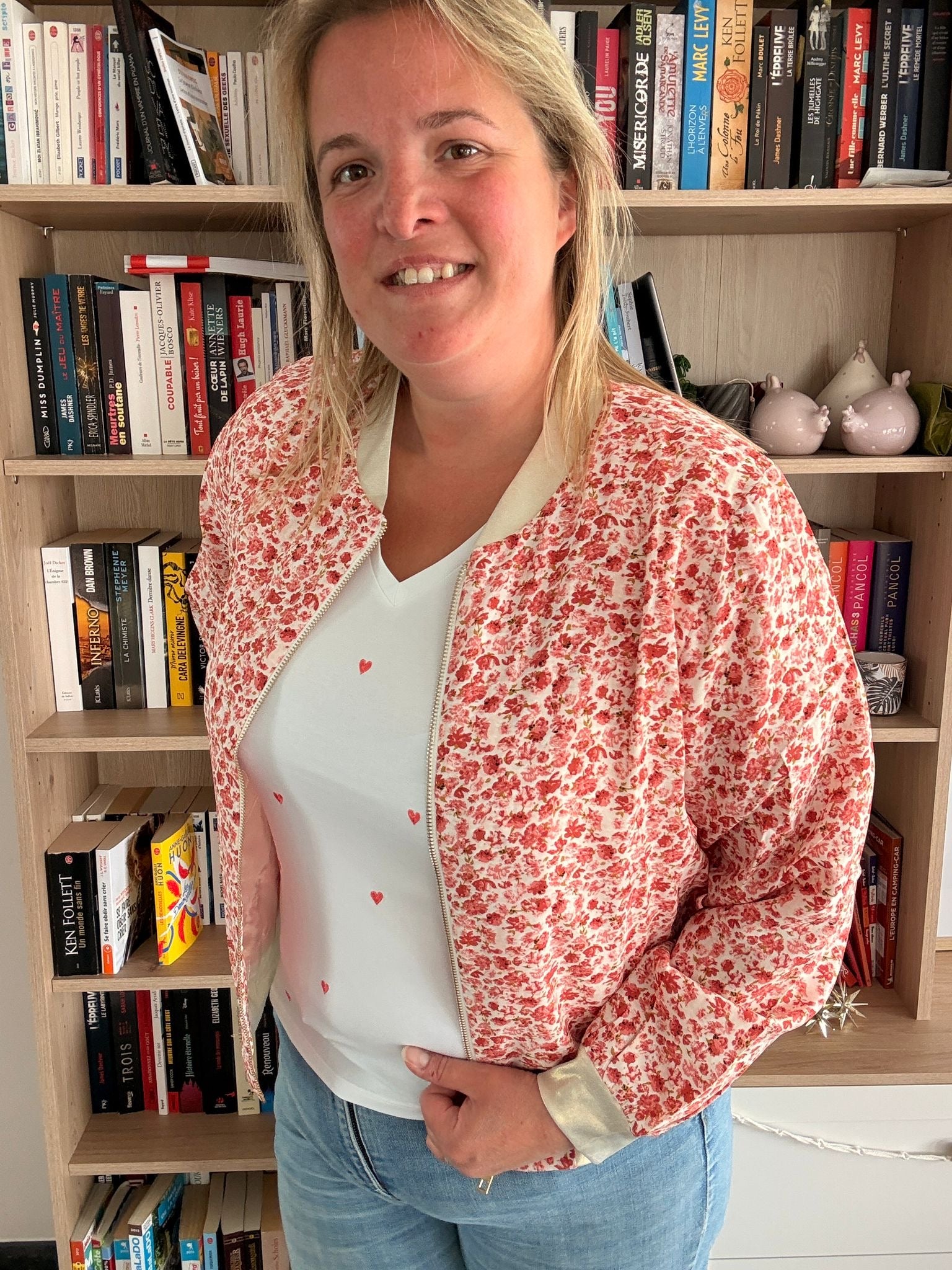 Bomber fleuri rouge orangé porté ouverte sur un t-shirt blanc, posé en pose décontractée dans une bibliothèque.