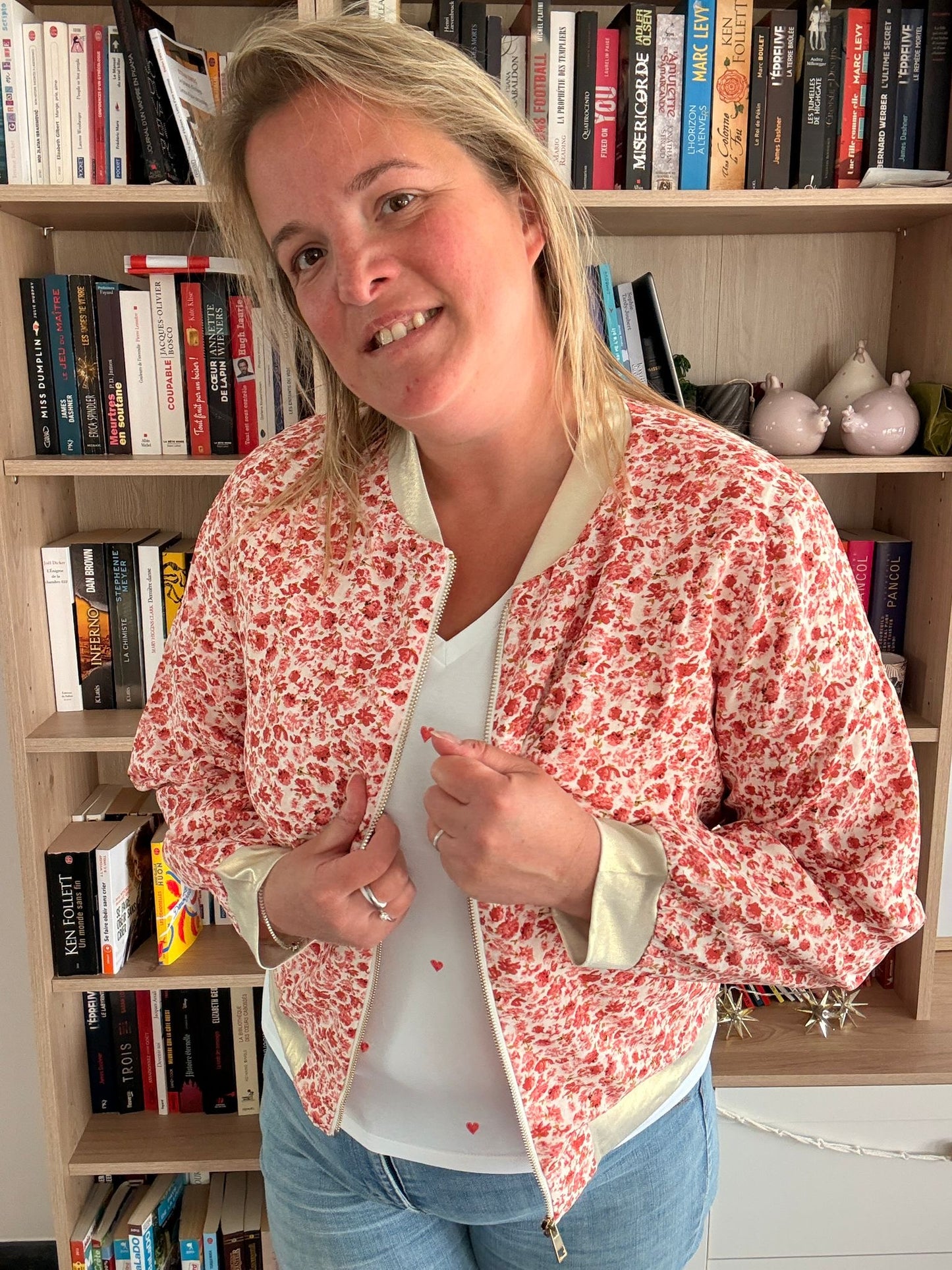 Veste bomber fleurie rouge et orangé portée par une femme, légère et romantique, dans une bibliothèque.