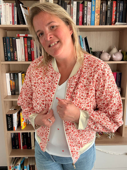 Veste bomber fleurie rouge et orangé portée par une femme, légère et romantique, dans une bibliothèque.