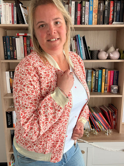Veste bomber fleurie rouge-orangé légère et féminine portée par une femme, dans une bibliothèque.