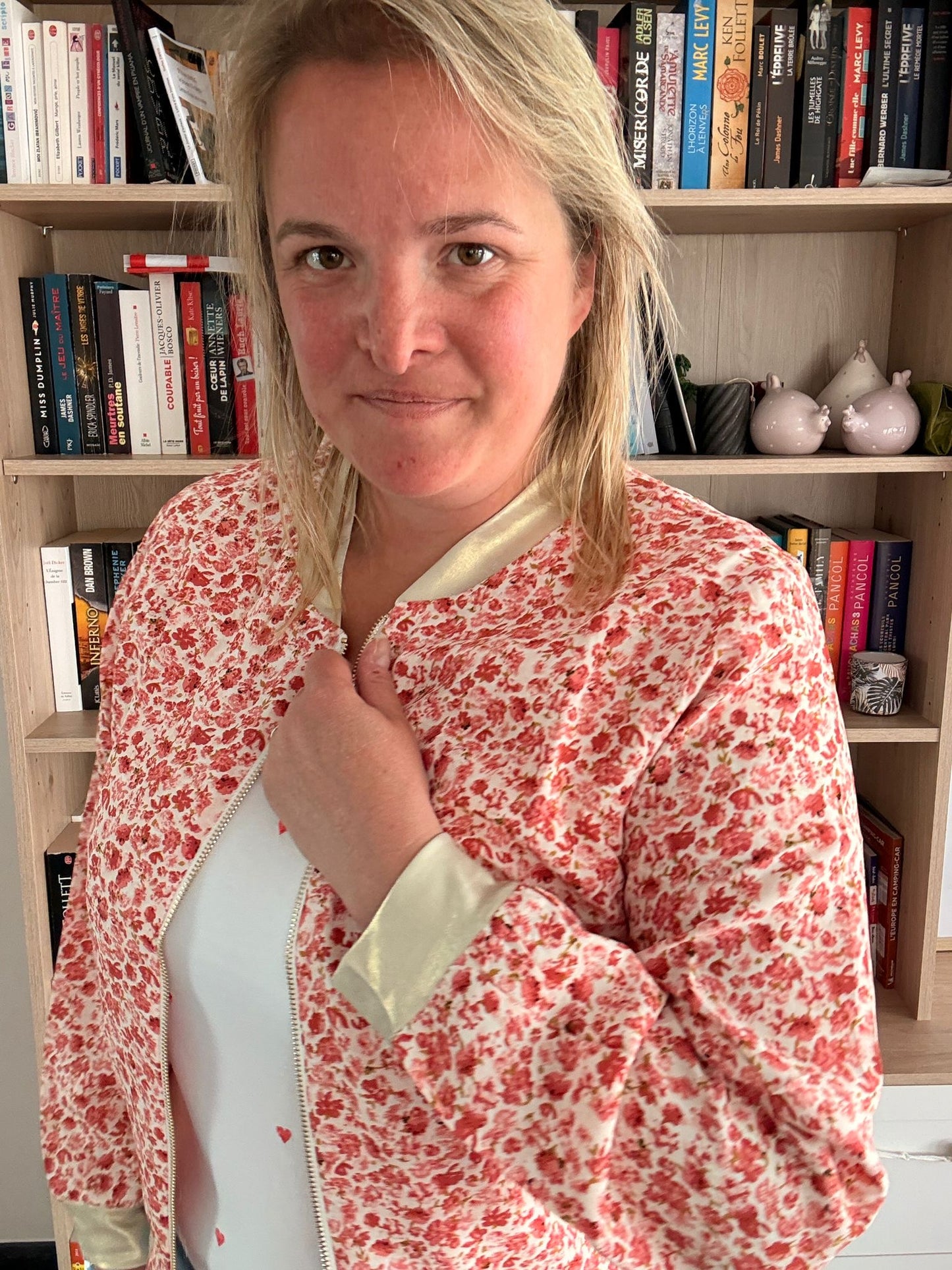 Veste légère à motif fleuri rouge et orangé portée par une femme devant une étagère de livres.