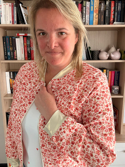 Veste légère à motif fleuri rouge et orangé portée par une femme devant une étagère de livres.