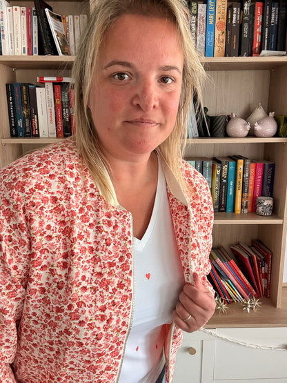 Veste légère à motif fleuri rouge-orangé portée par une femme devant une étagère de livres.