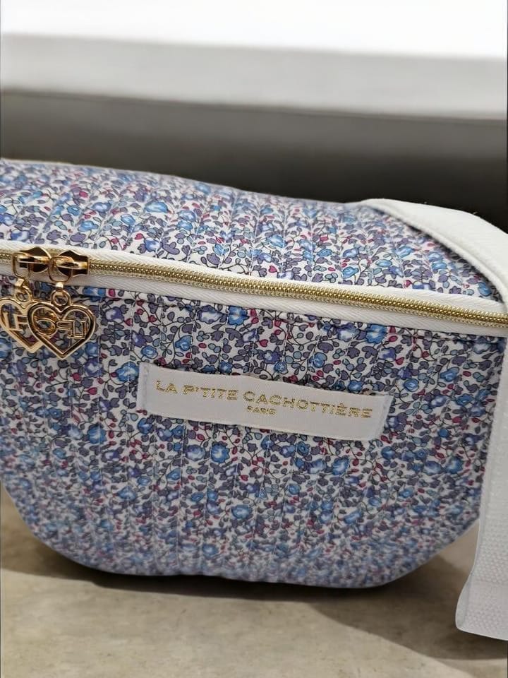Sac banane floral Liberty rouge La Ptite Cachottière avec fermeture éclair dorée et porte-clé cœur gravé posé sur fond clair.