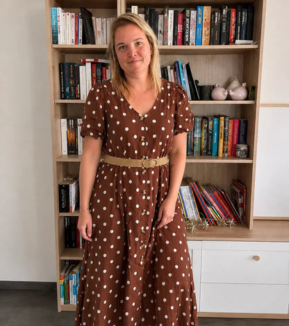 Robe midi femme à pois beige et marron portée par une femme, manches bouffantes, col en V, ceinture ceinturée beige, style vintage.