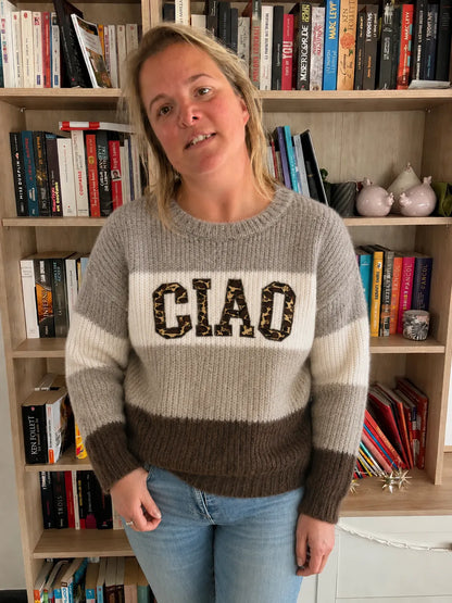 Pull en maille femme CIAO gris marron portée par une femme devant une étagère remplie de livres.