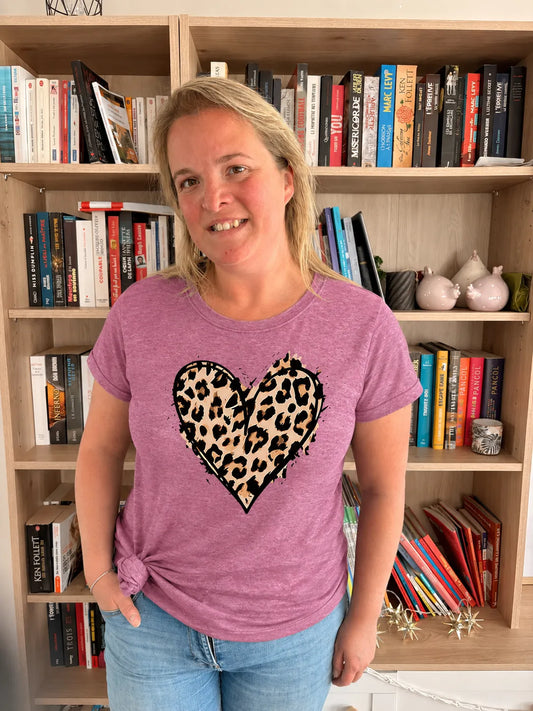 T-shirt rose casual chic imitant imprimé léopard en cœur sur une femme souriante devant des étagères de livres.