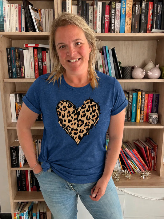 T-shirt bleu femme avec cœur imprimé léopard, portée par une femme, debout devant une étagère de livres.