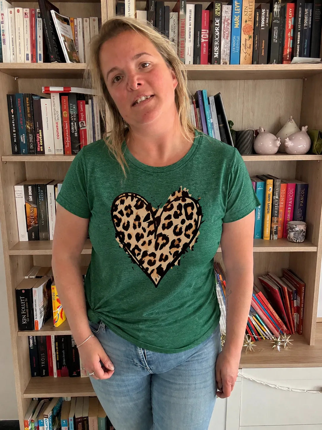 T-Shirt Vert Col Rond Femme avec motif cœur Léopard, porté par une femme devant une étagère de livres.