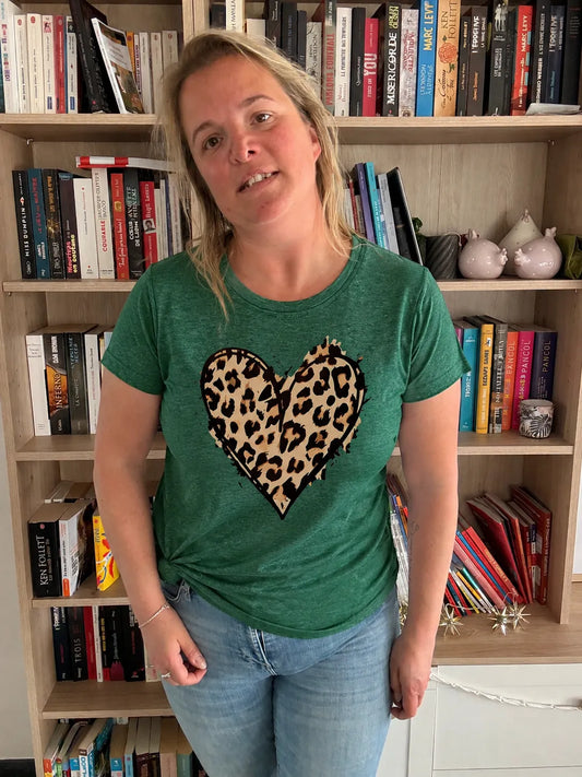T-Shirt Vert Col Rond Femme avec motif cœur Léopard, porté par une femme devant une étagère de livres.