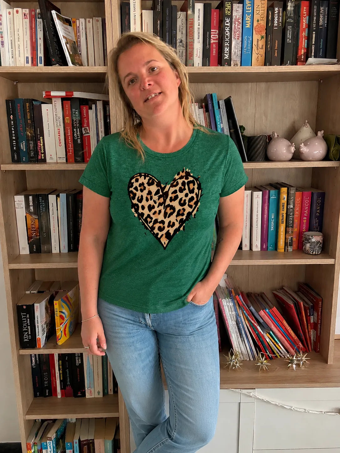 T-shirt Vert à col rond femme avec motif cœur léopard, portée par une femme debout dans une bibliothèque.