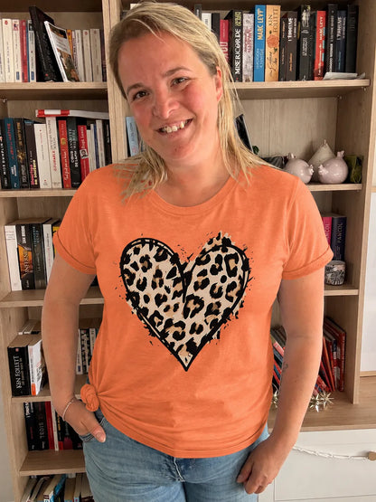 T-shirt femme orange avec imprimé cœur léopard noir et beige, col rond, porté par une femme souriante dans une bibliothèque.