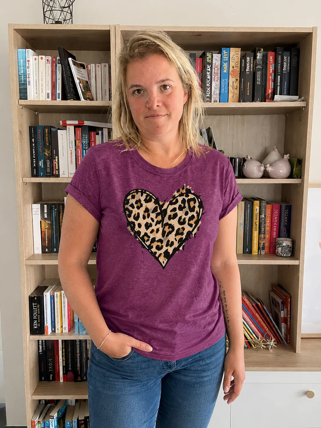 T-shirt femme violet avec cœur imprimé léopard au centre, portée par une femme devant une bibliothèque.