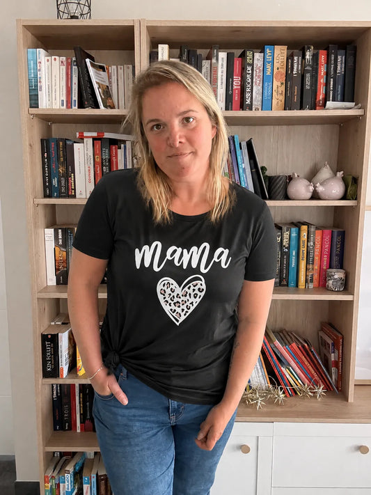 T-shirt noir femme avec le mot « Mama » et un cœur léopard, porté par une femme devant une bibliothèque.