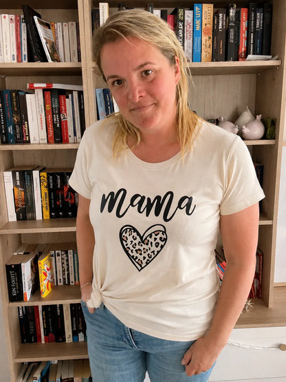 T-shirt blanc femme Mama cœur léopard, modèle porté par une femme devant une étagère de livres.