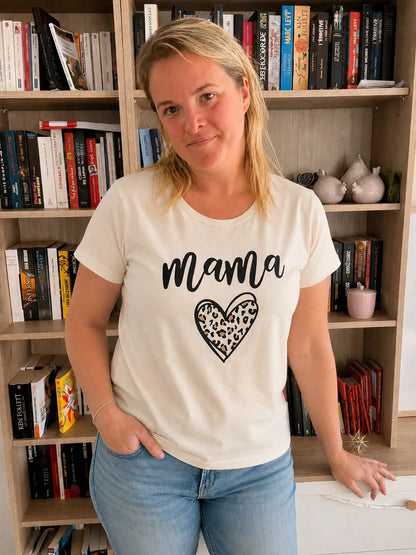 T-Shirt blanc avec cœur léopard et texte Mama, femme debout près d’une étagère de livres.