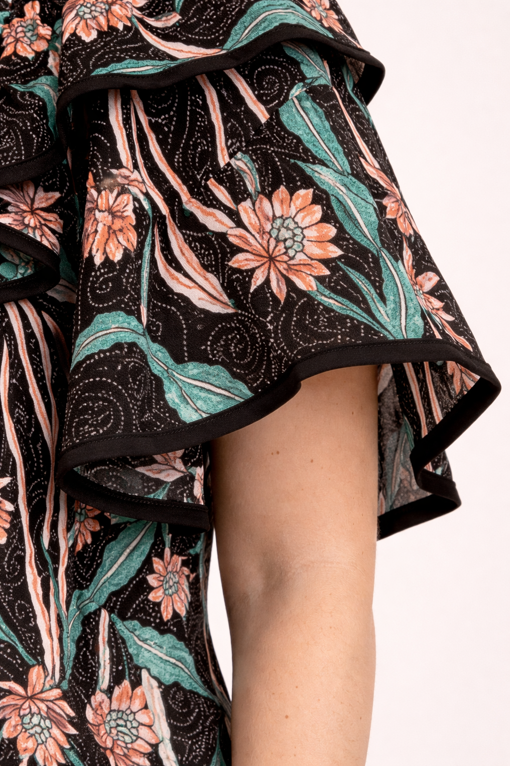 Blouse fluide noire à motif floral orange et vert, manches volantes avec bordure noire.