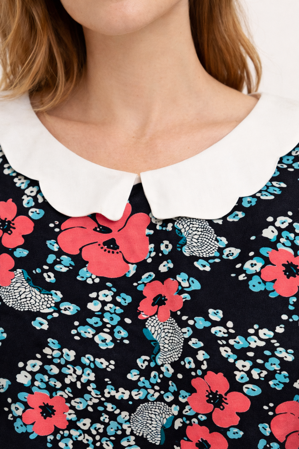 Blouse fluide à col Claudine blanche sur fond marine à motifs floraux rouges et bleus, près du décolleté.