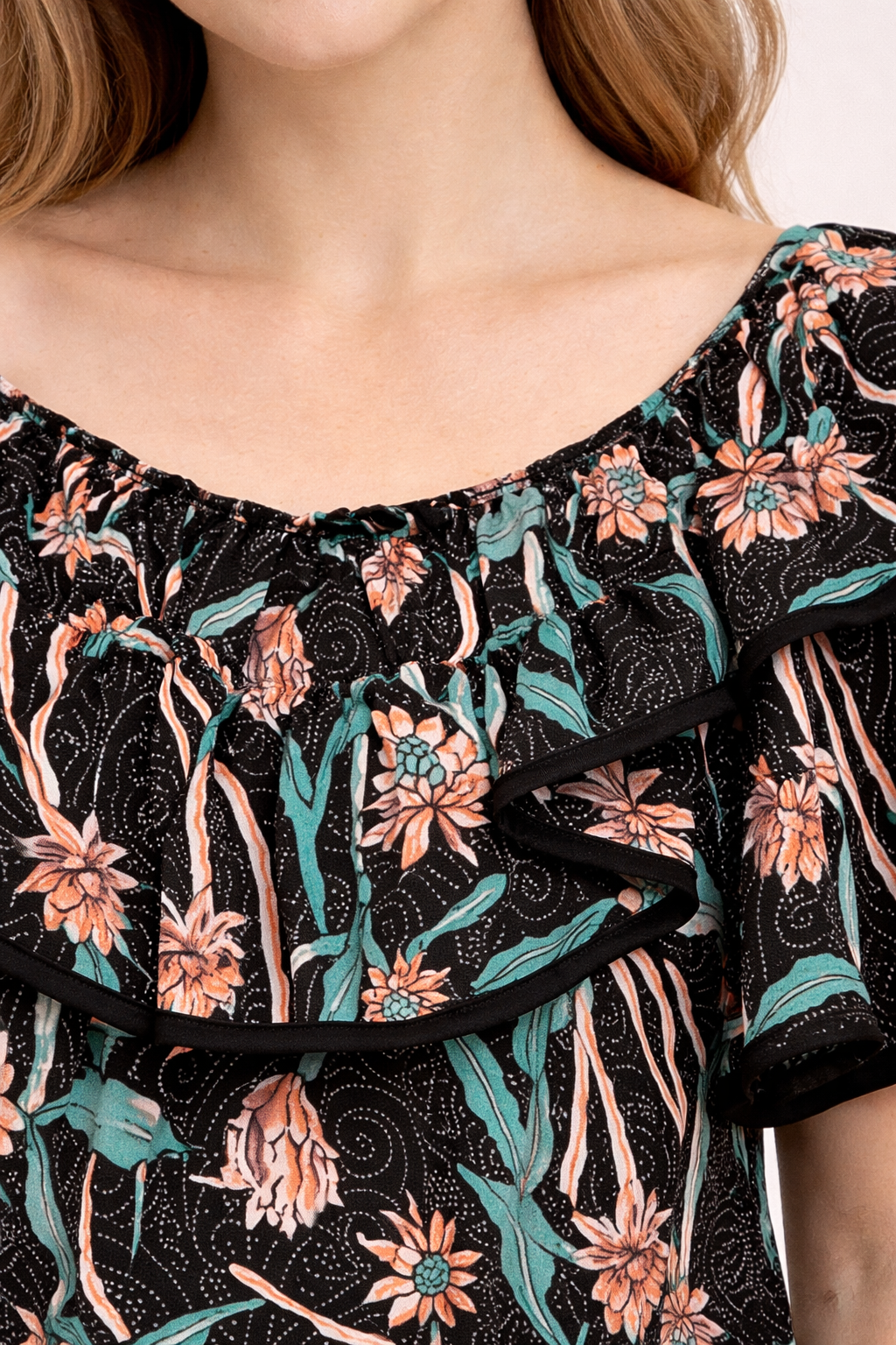 Blouse noire à motif floral pêche et vert avec col volanté et double ruche noir sur les bords.