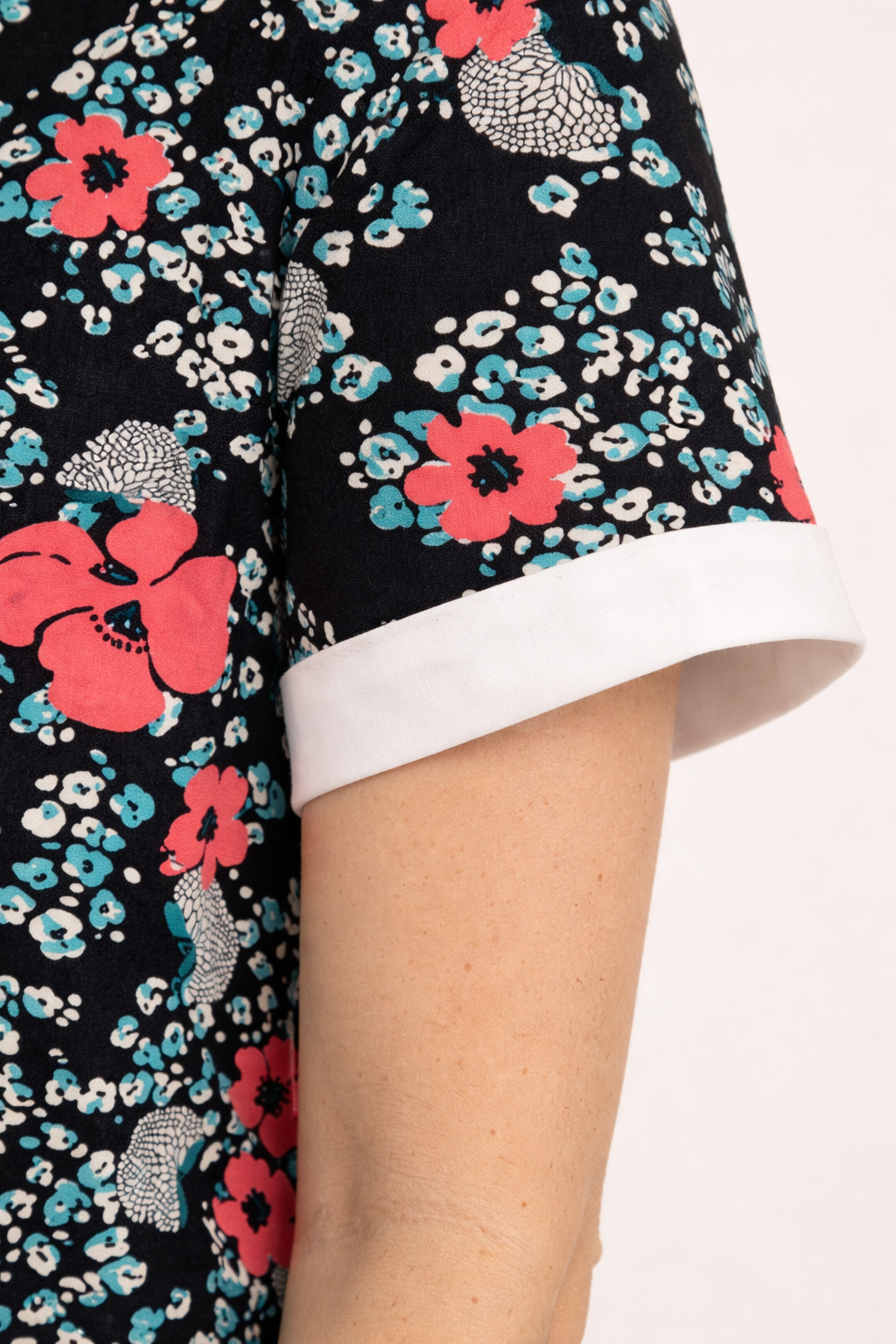Blouse florale noire à manches courtes retroussées avec revers blanc, motif fleurs roses et bleues.