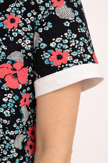Blouse florale noire à manches courtes retroussées avec revers blanc, motif fleurs roses et bleues.
