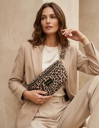 Sac banane matelassée léopard portée en ceinture par une femme en outfit beige, réglable et chic.