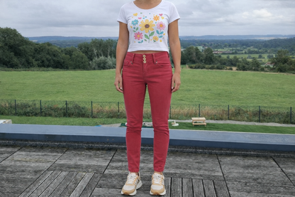 Jeans skinny taille haute rouge brique de Le Petit Placard porté par une femme en tenue fleurie sur une terrasse.