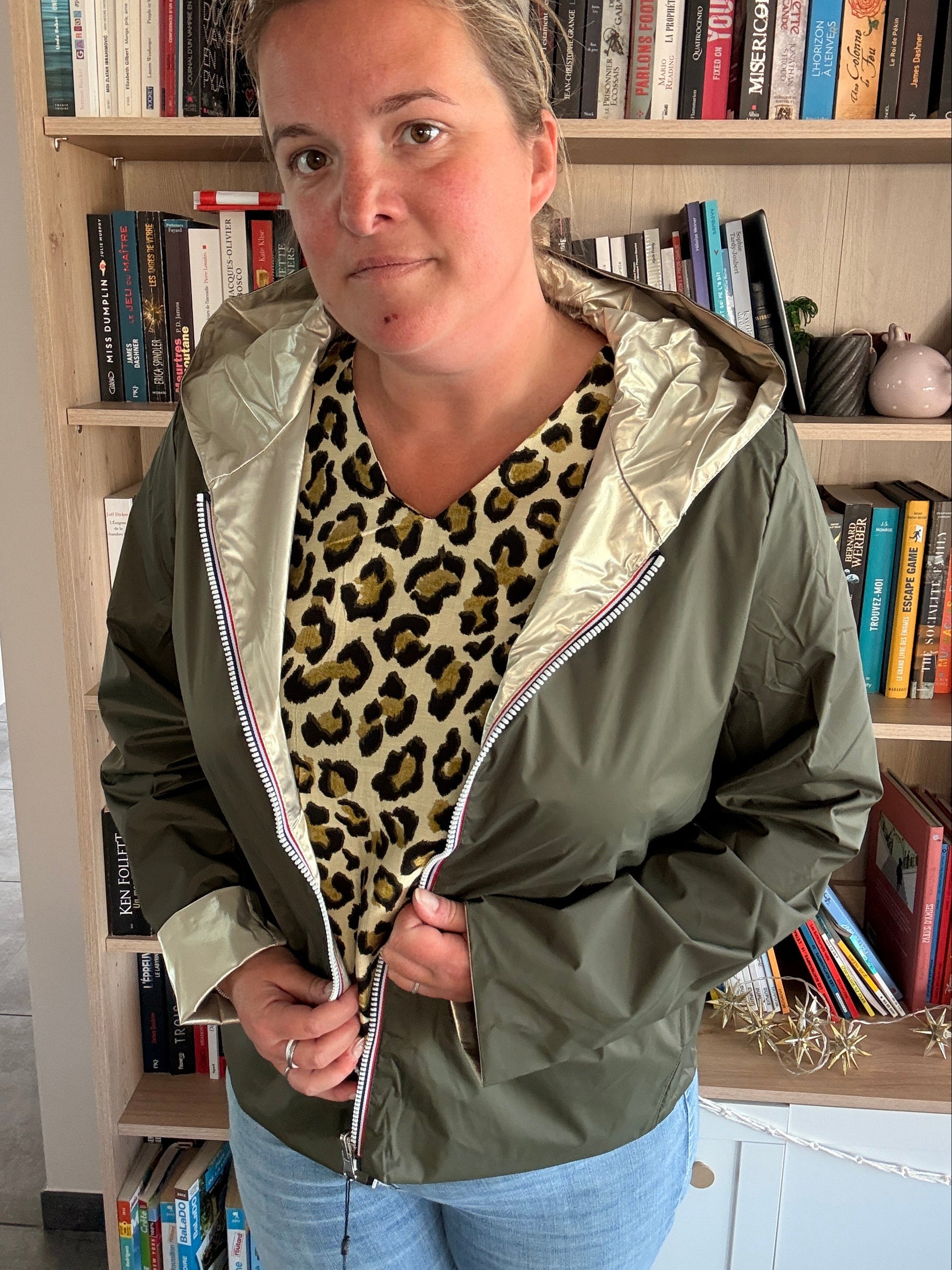 Imperméable réversible court kaki/doré porté par une femme, veste légère avec doublure dorée et capuche, livreurs en arrière-plan.