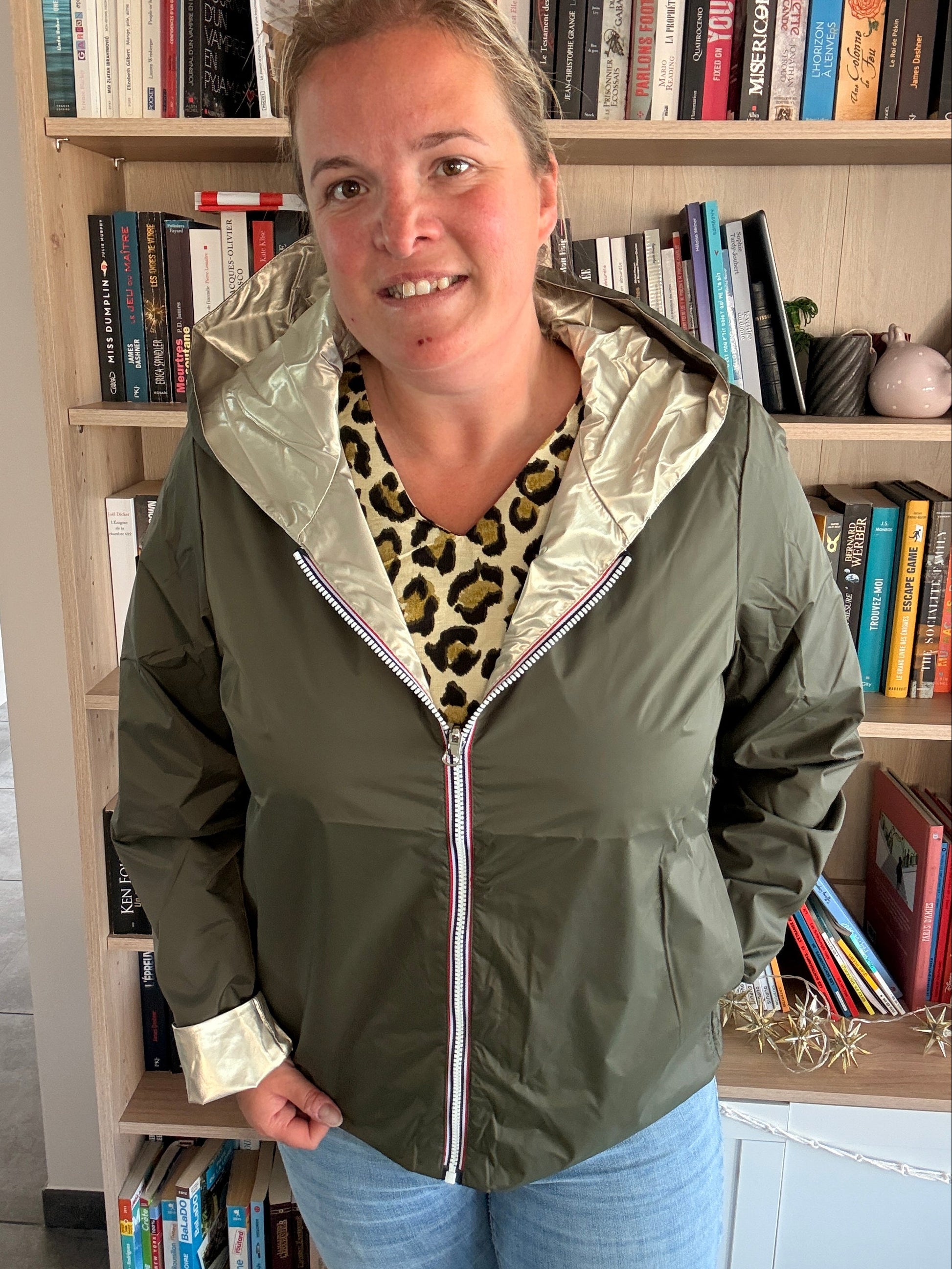 Imperméable réversible kaki/doré porté par une femme dans une bibliothèque, col et ourlet dorés, zippé, veste légère Laura Jo.