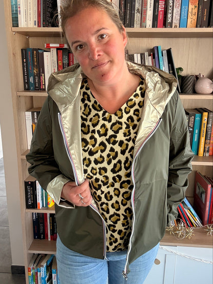 Imperméable réversible court kaki/doré porté par une femme, veste légère ouverte sur un pull léopard et jean, en intérieur.