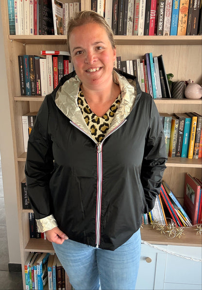 Imperméable réversible court Laura Jo porté par une femme souriante, noir/doré, doublure et col doré, posé devant une étagère de livres.