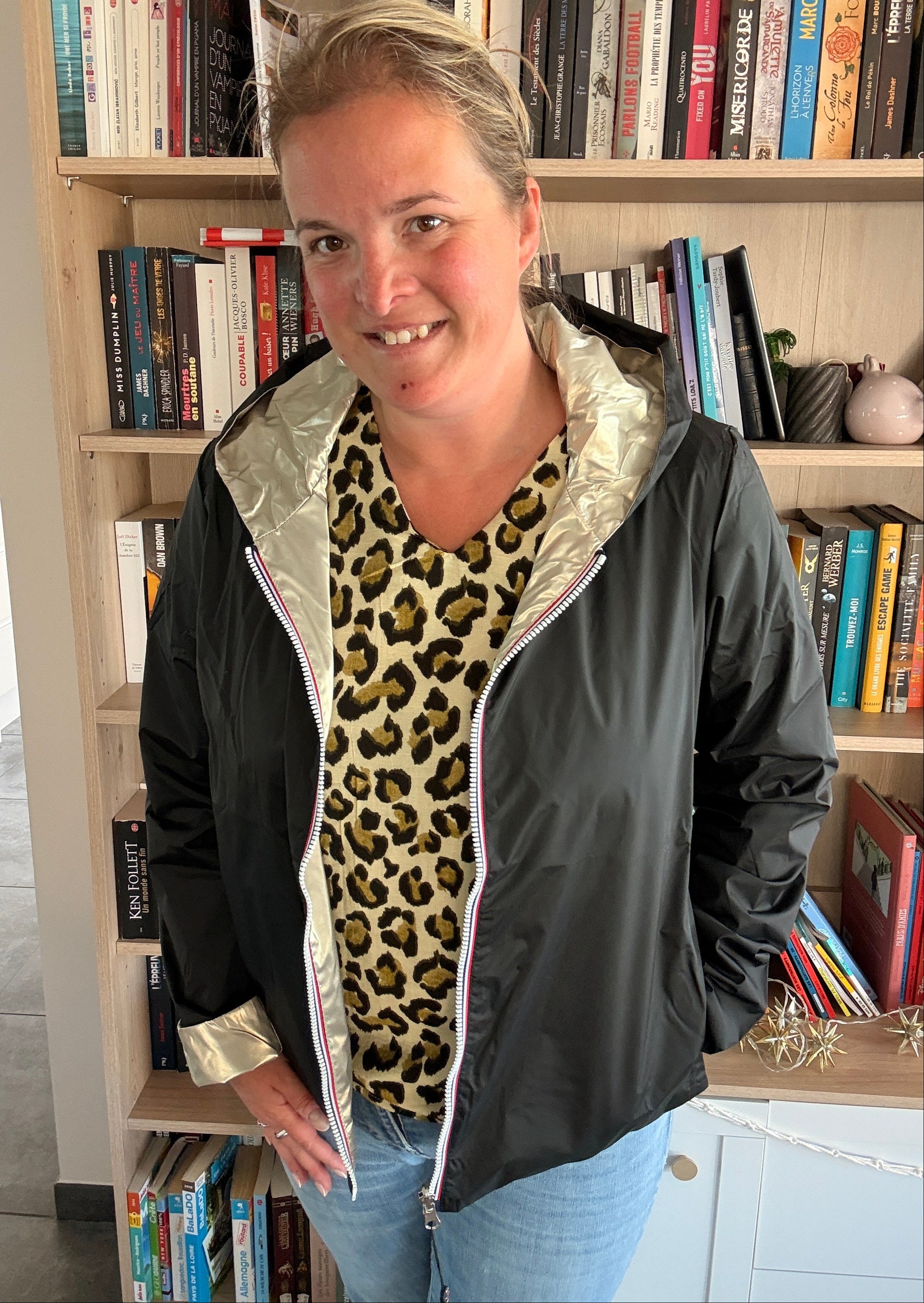 Imperméable réversible court Laura Jo porté par une femme en intérieur, noir et doré, doublure argentée, avec chemise à motif léopard et jeans.