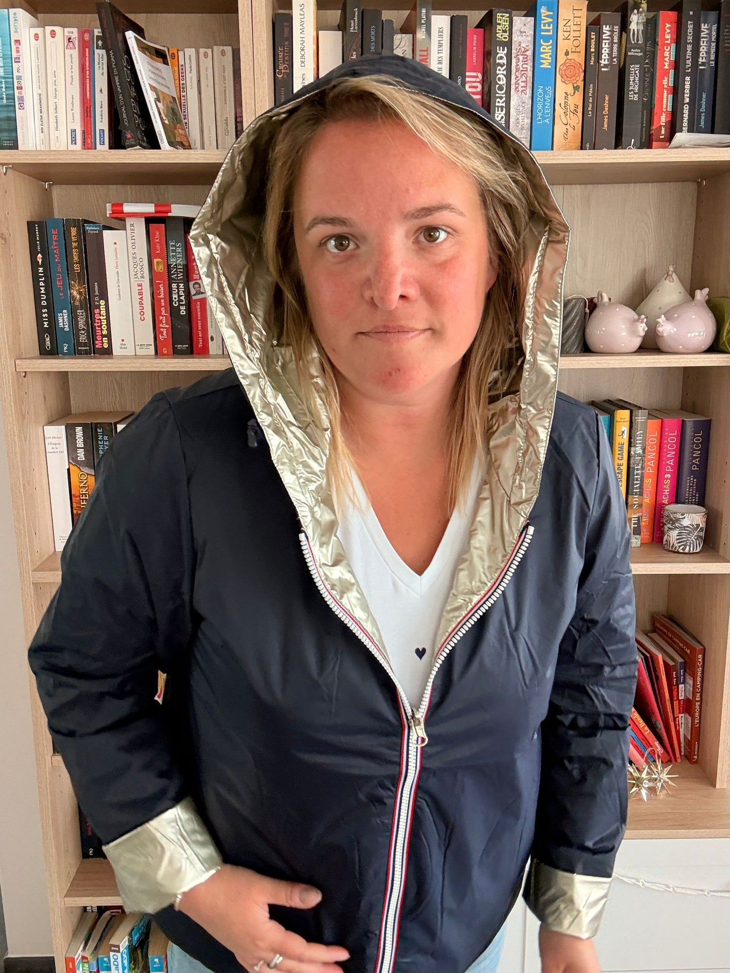 Imperméable réversible court bleu marine doré femme, modèle Laura Jo Mi Saison, porté par une femme devant une bibliothèque.