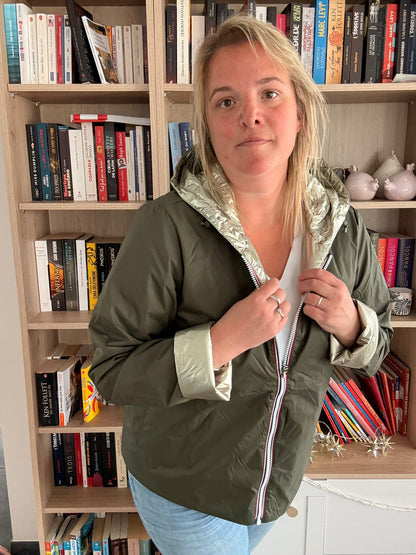 Femme portant un imperméable réversible court kaki doré, debout à côté d'une bibliothèque, en train de tenir les colliers de fermeture zippée sur le devant.