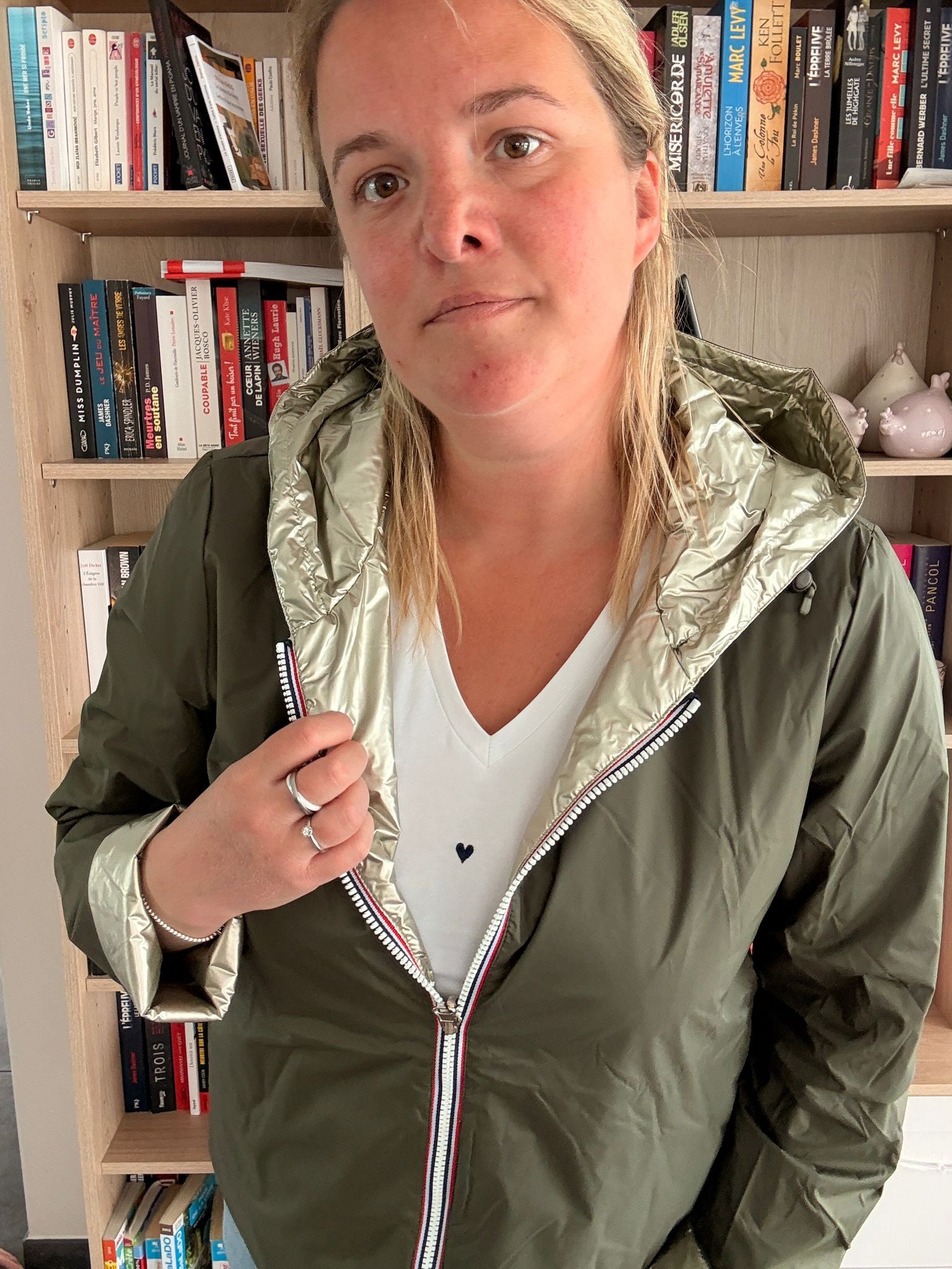 Imperméable réversible court kaki doré femme portée en intérieur, avec capuche, zip doré et doublure lumineuse. Laura Jo Mi-Saison.