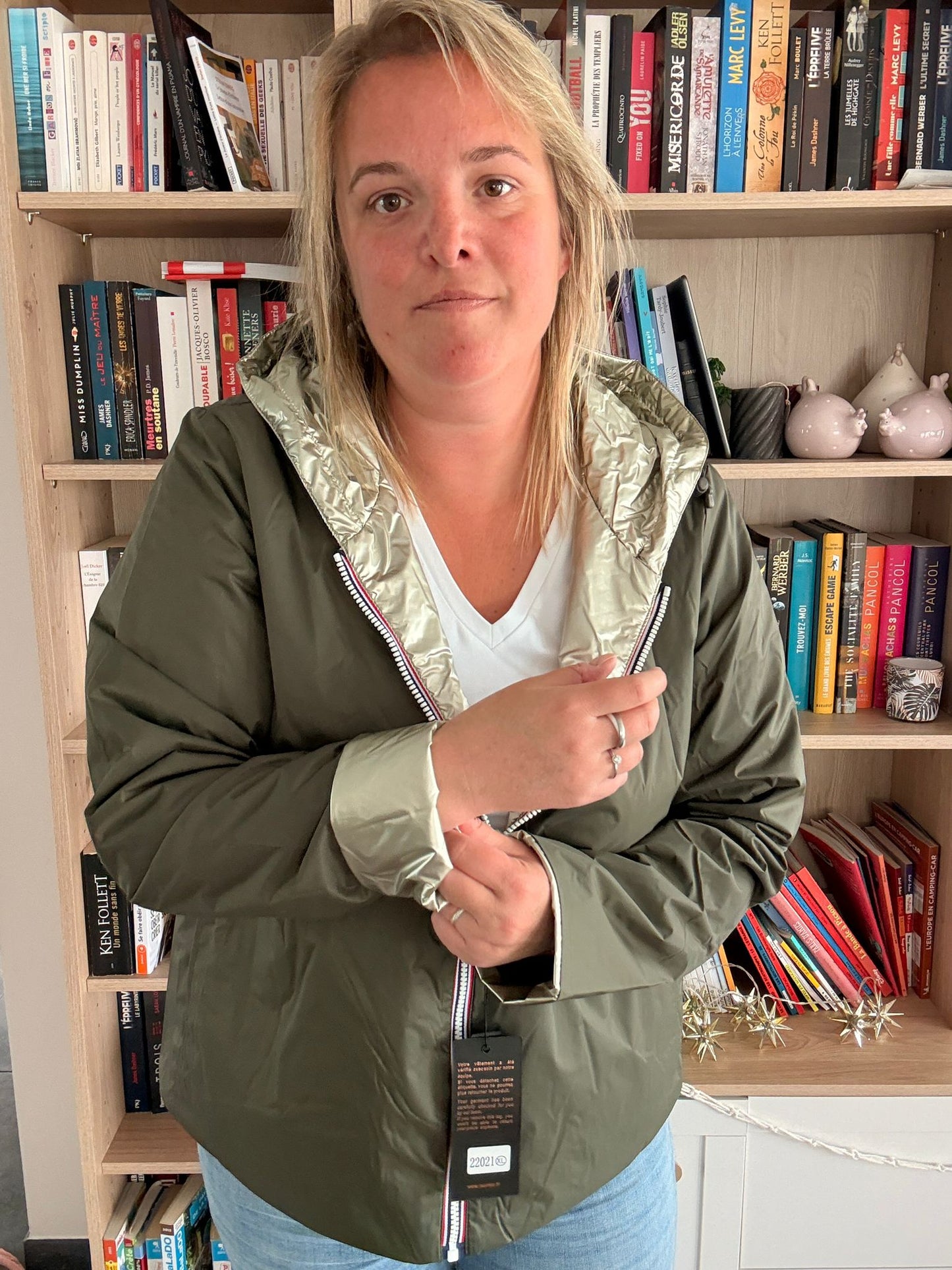 Imperméable réversible court kaki doré femme Laura Jo Mi-Saison portée par une femme devant une étagère de livres.