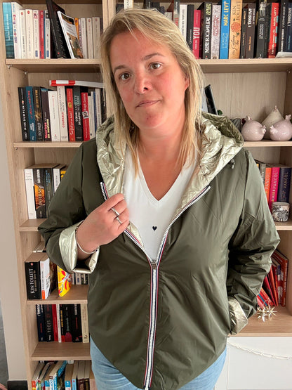 Imperméable réversible court kaki doré pour femme porté par une personne tenant la fermeture, en intérieur avec bibliothèque en arrière-plan.