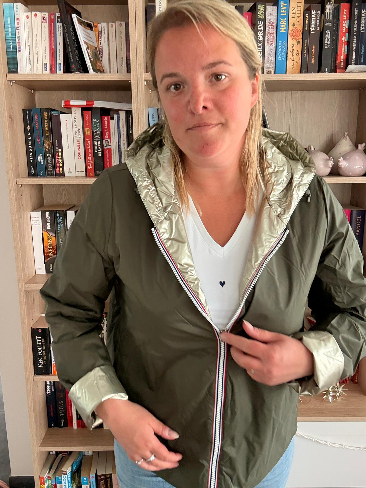 Imperméable réversible court kaki doré femme Laura Jo Mi-Saison porté en intérieur, ouverte sur un pull blanc; étagères de livres en arrière-plan.