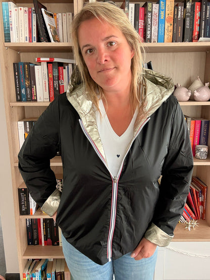 Imperméable réversible court noir doré femme Laura Jo Mi-Saison : femme posant devant bibliothèque, veste noire avec capuche dorée et ourlets dorés, zippé, jeans bleu.