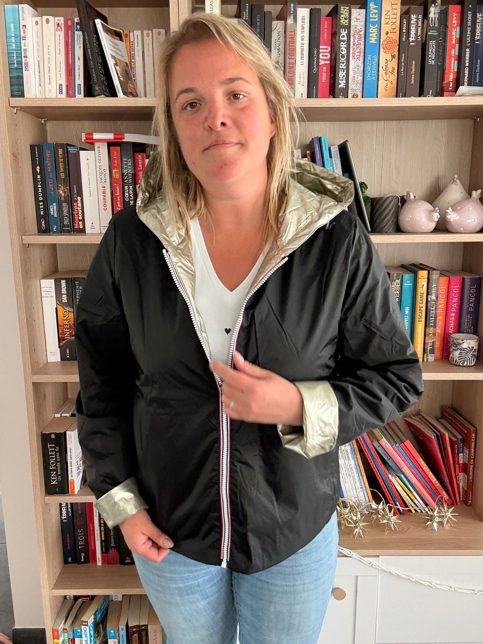 Imperméable réversible court noir doré femme Laura Jo Mi-Saison portée par une femme devant une étagère remplie de livres.
