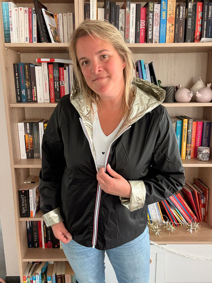 Imperméable réversible court noir doré pour femme, portée par une jeune femme dans une pièce avec étagères et livres. Laura Jo Mi-Saison.