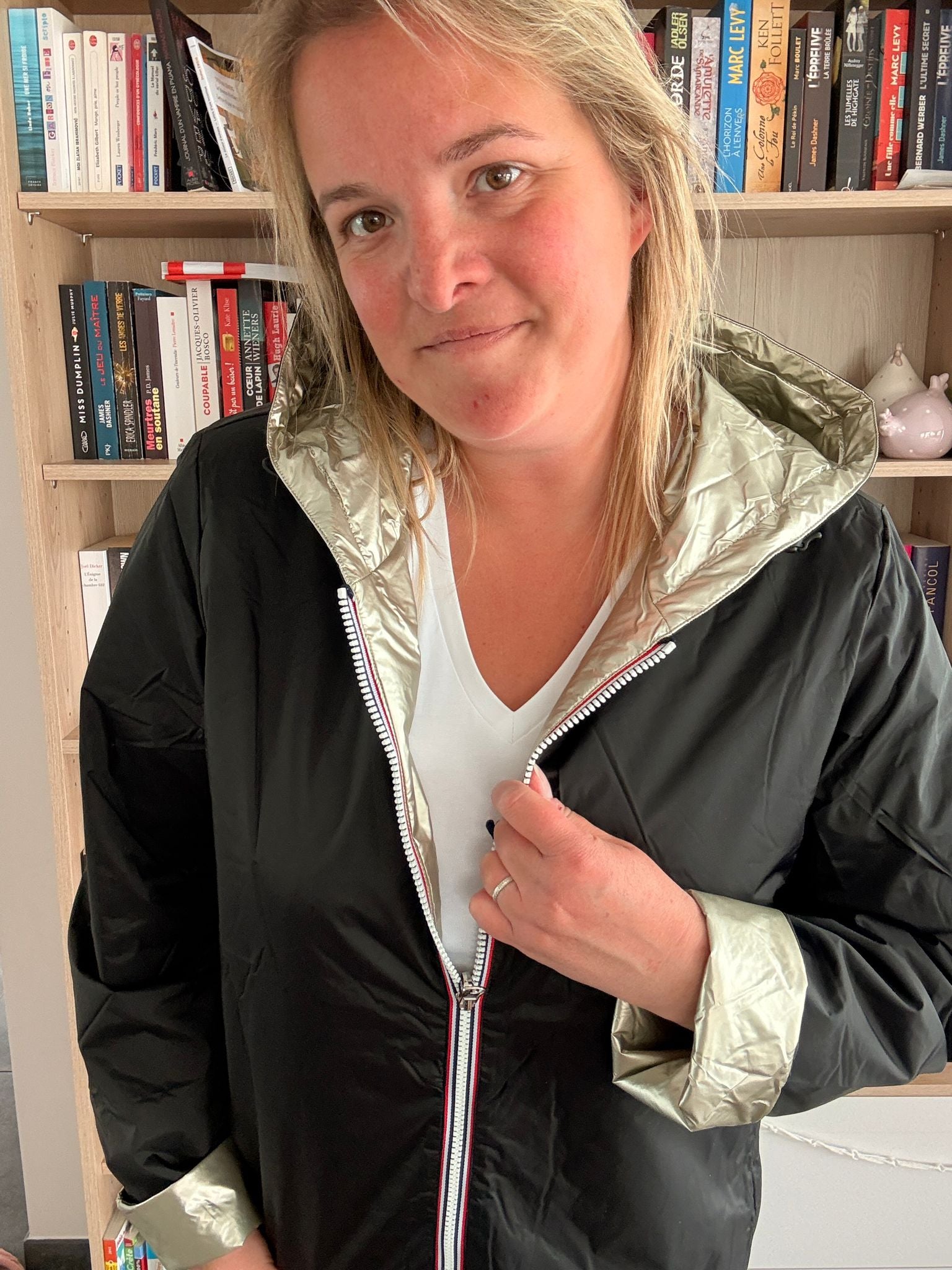 Manteau imperméable réversible court noir doré pour femme, porté femme devant bibliothèque. Laura Jo Mi-Saison.