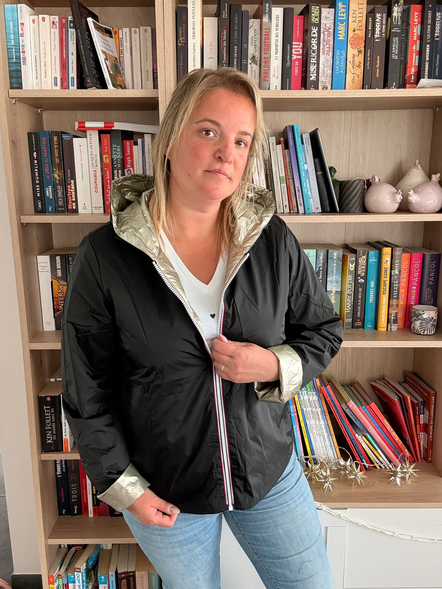 Imperméable réversible court noir doré pour femme, portée par une femme dans une bibliothèque.