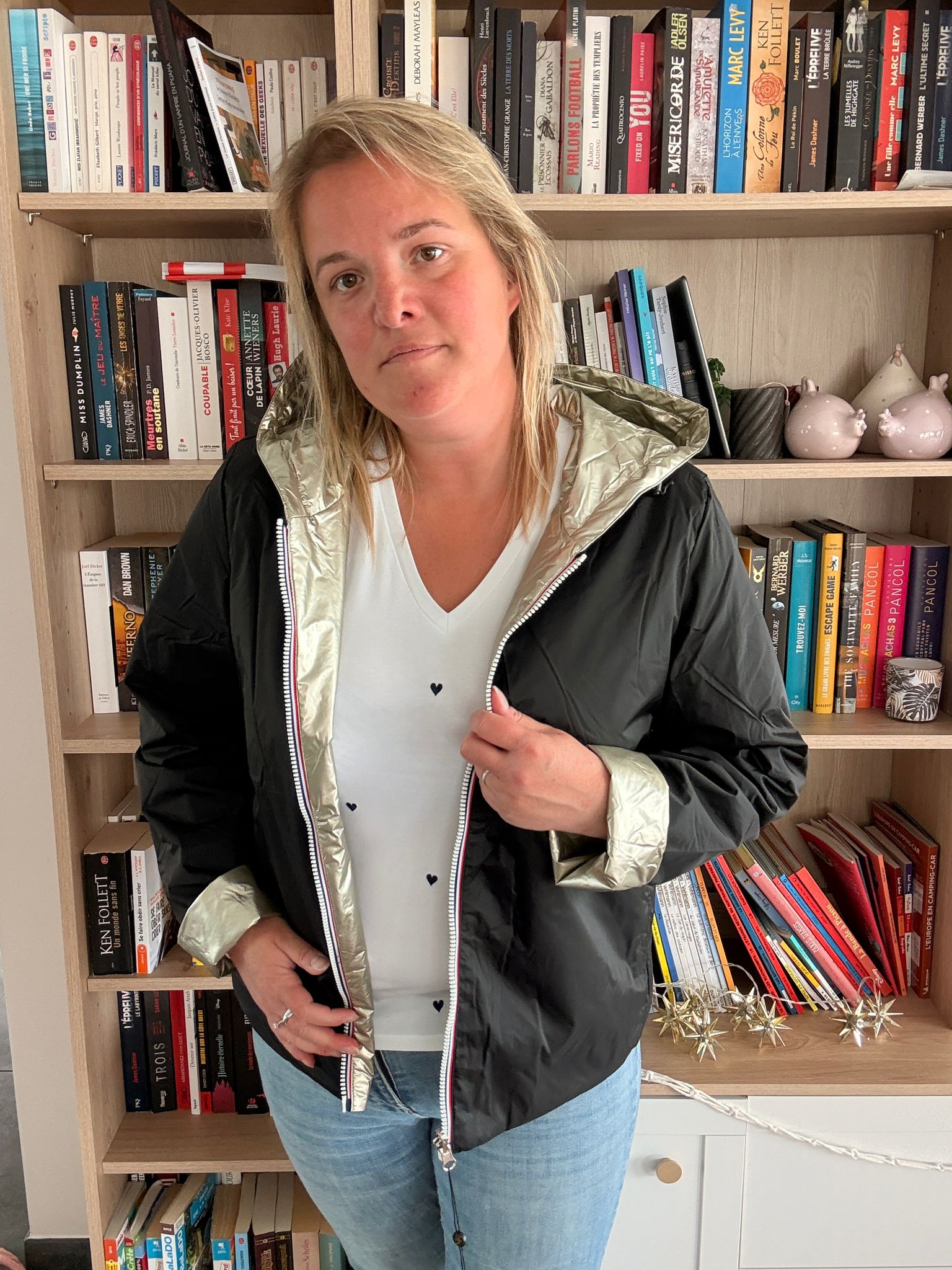 Imperméable réversible court noir doré pour femme porté par une personne devant une étagère de livres.