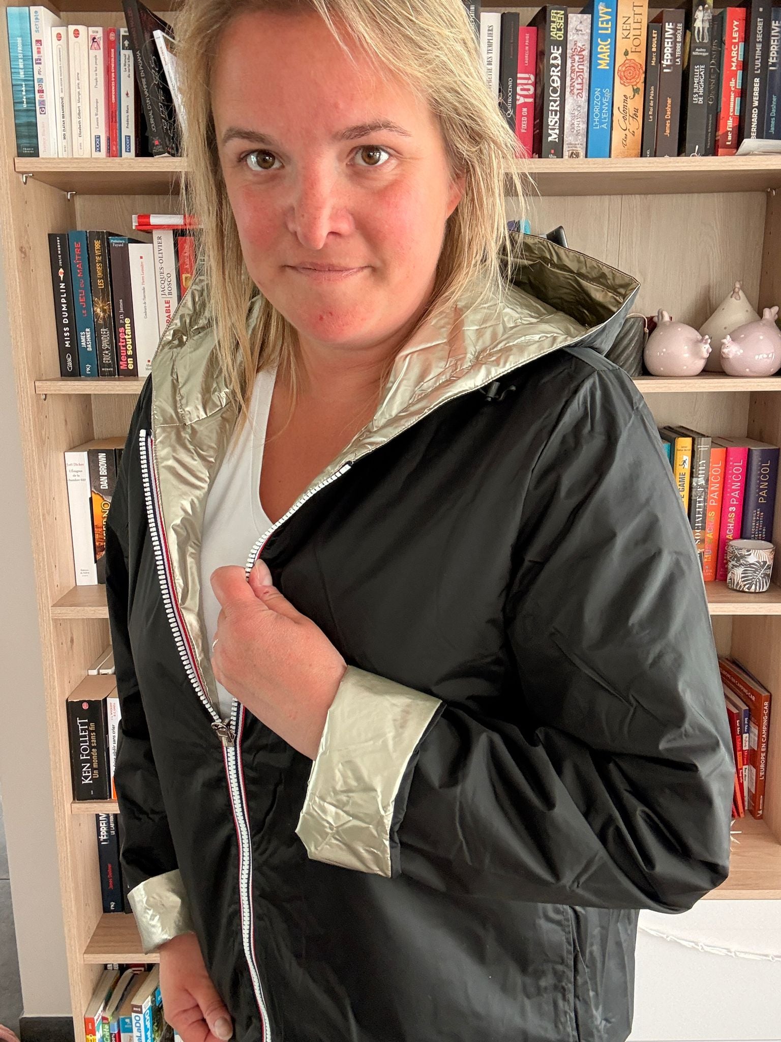 Imperméable réversible court noir doré femme Laura Jo Mi-Saison portée par une femme amoureuse des livres, intérieur doré brillant, extérieur noir mat.