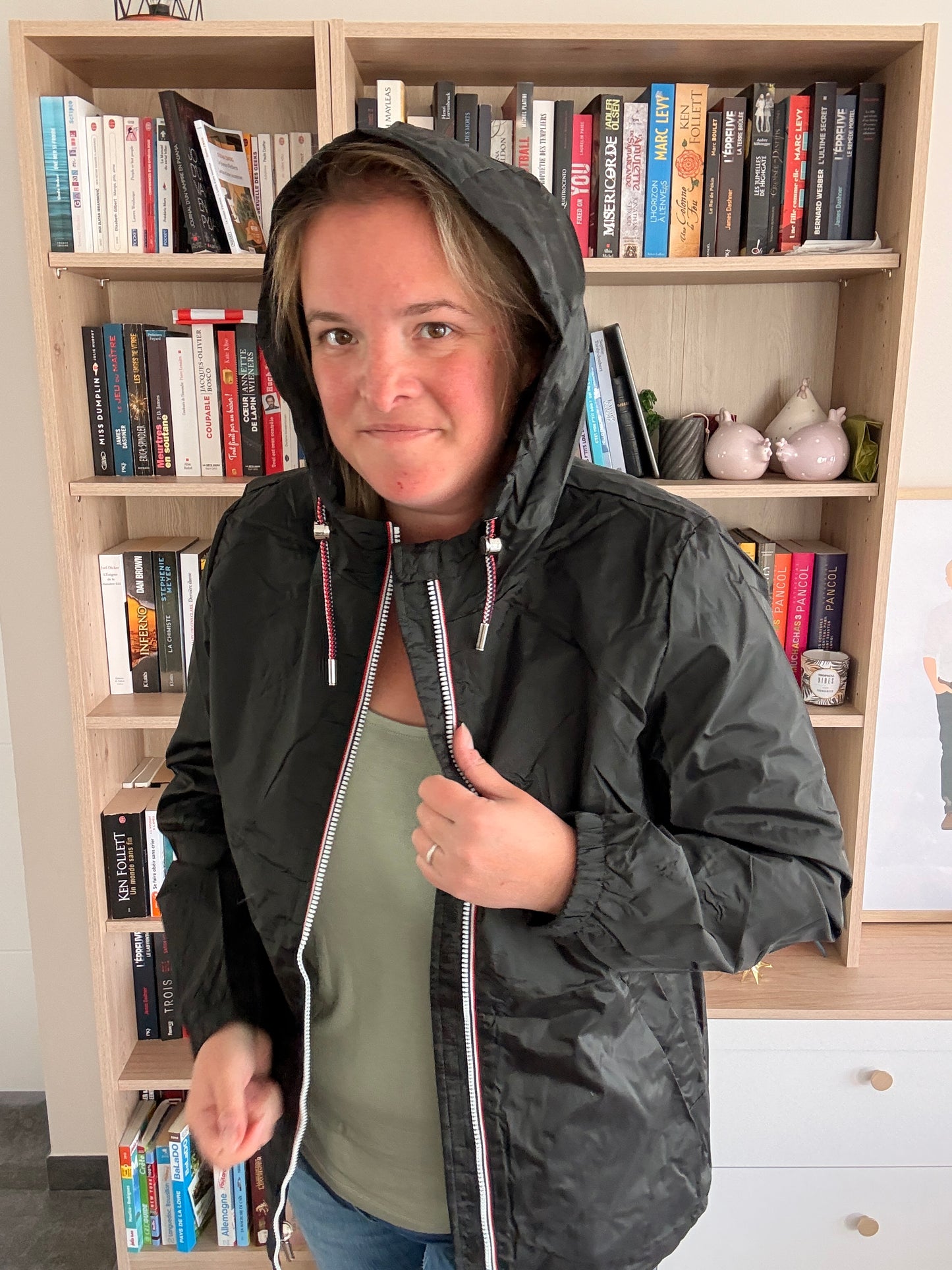 Femme portant l'imperméable court noir Laura Jo avec capuche relevée, cordons tricolores ajustables visibles, veste ouverte